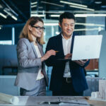 A team of multiracial business architects and designers discuss creating a project draft drawing by looking at laptop monitor screen a computer desk. Asian male and female developers together teamwork