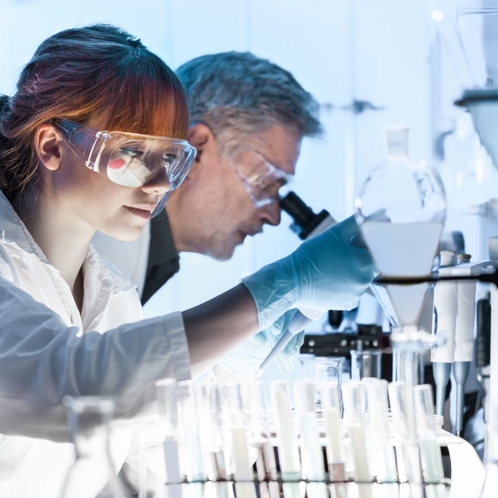 Health care researchers working in life science laboratory. Young female research scientist and senior male supervisor preparing and analyzing microscope slides in research lab.