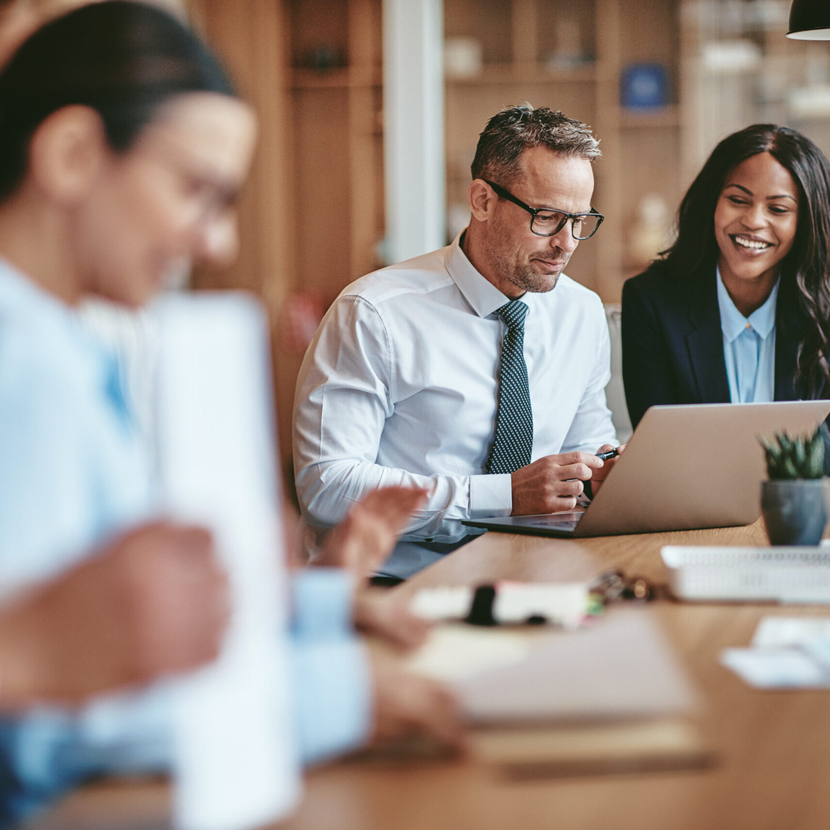 Two diverse businesspeople smiling while working on a laptop together at the end of a boardroom table in an office